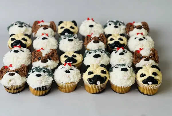 Dog face cupcakes piped in buttercream as pugs, terriers, sheepdogs and huskies with red bows