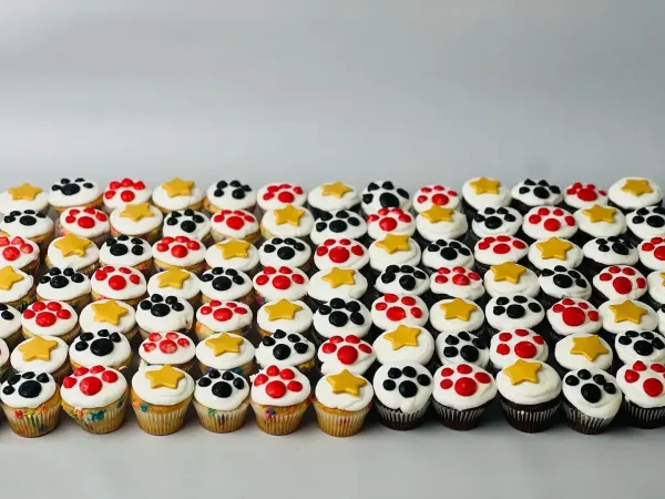 Mini cupcakes with white icing and piped red and black paw prints with gold fondant stars