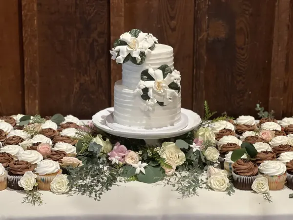 Two-tier white cake with sugar gardenias above white and chocolate cupcakes with roses and eucalyptus