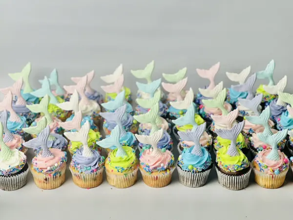 Rows of cupcakes topped with pastel fondant mermaid tails and sprinkle-rimmed buttercream