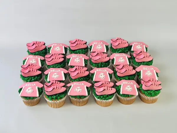 Soccer cupcakes with green grass frosting, pink fondant cleats and jerseys reading Bella 4