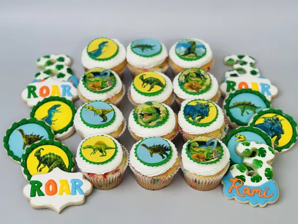 Dinosaur cupcakes with printed toppers beside iced cookies reading Roar, Rami and the number 3