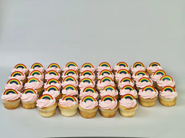 Mini cupcakes with pink frosting swirls, fondant rainbows and small piped white clouds