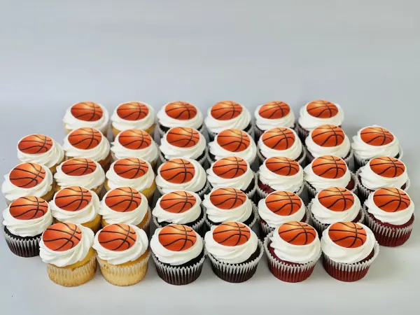 Cupcakes with white frosting swirls and printed basketball toppers on vanilla, chocolate and red velvet