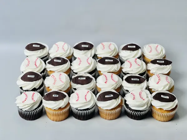 Cupcakes with white frosting and fondant footballs and stitched baseballs