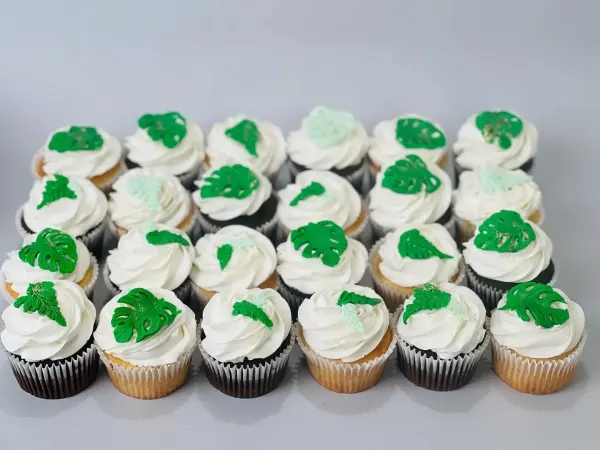 Cupcakes with white frosting swirls topped with green fondant monstera and fern leaves