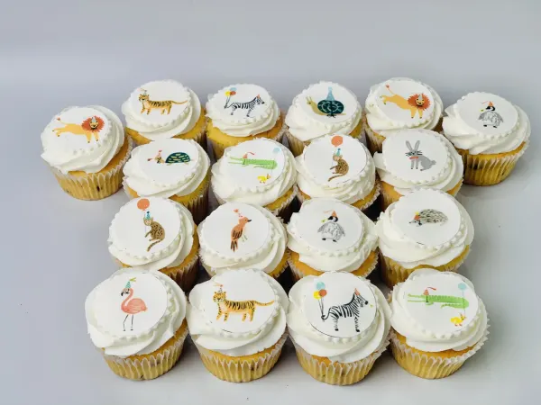 White buttercream cupcakes with edible prints of party-hat animals including a lion, zebra and flamingo