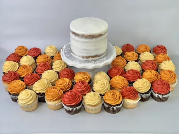 Semi-naked white buttercream cake ringed by cupcakes swirled in red, orange and yellow buttercream