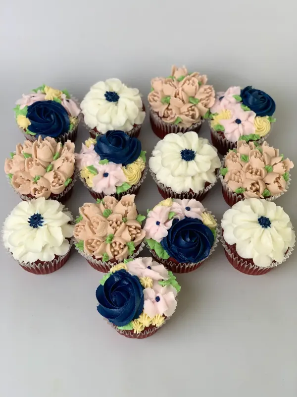 Red velvet cupcakes piped with navy roses, cream anemones and peach tulip clusters