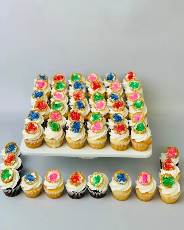 White swirl cupcakes topped with rock candy geode discs in blue, red, green and pink with gold edges