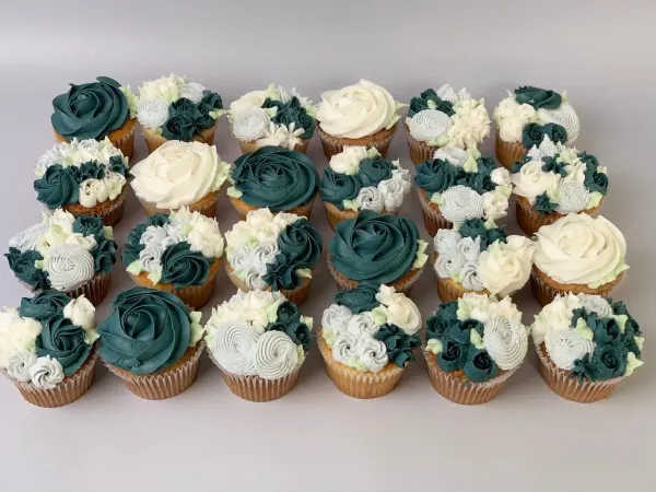 Cupcakes piped with dark teal and ivory buttercream roses and small flower clusters