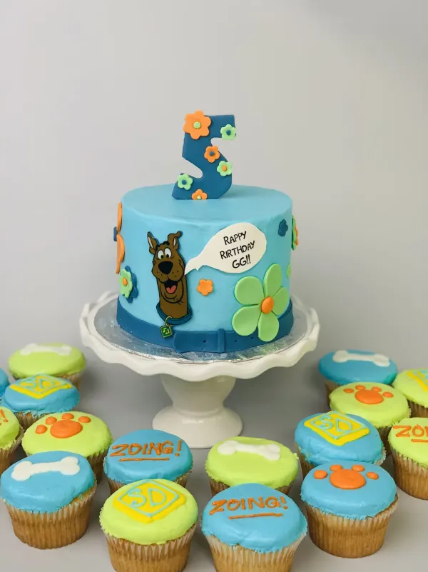 Blue cake with a cartoon dog, number 5 and Happy Birthday GG bubble, with bone and paw print cupcakes