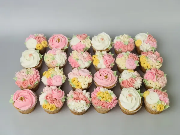 Cupcakes piped with pink, ivory and yellow buttercream roses and blossom clusters with gold pearls