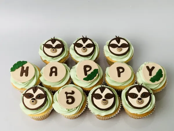 Green buttercream cupcakes with fondant sloth faces spelling HAPPY and a number 5