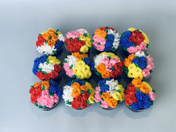 Twelve cupcakes piped as buttercream flower bouquets in red, pink, blue, yellow and orange