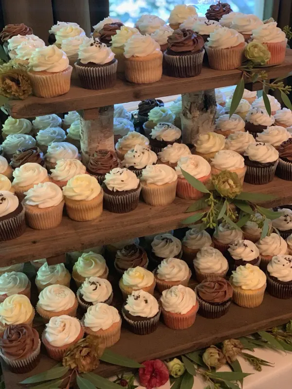 Wooden tiered stand of white and chocolate buttercream cupcakes with eucalyptus and flowers