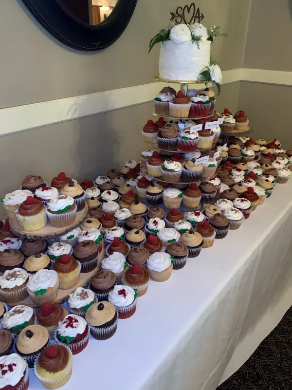 White textured cake with an SMA monogram topper above a table of labeled flavor cupcakes