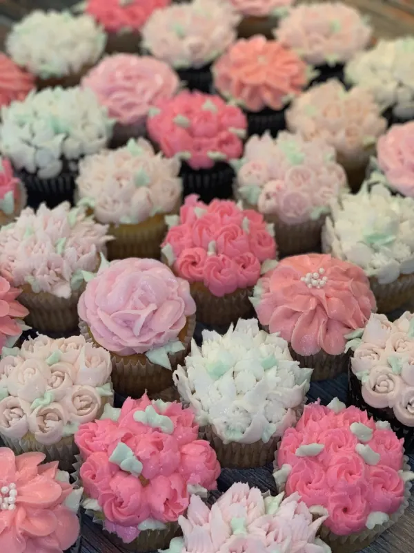 Cupcakes piped with pastel pink, peach and white buttercream flowers and mint green leaves