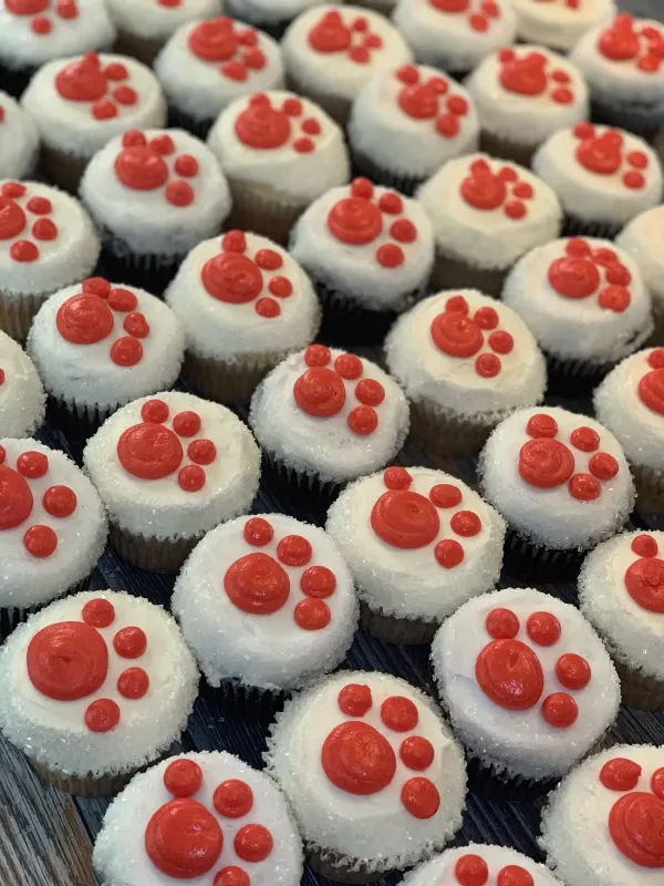 White buttercream cupcakes edged in sanding sugar with red piped paw prints