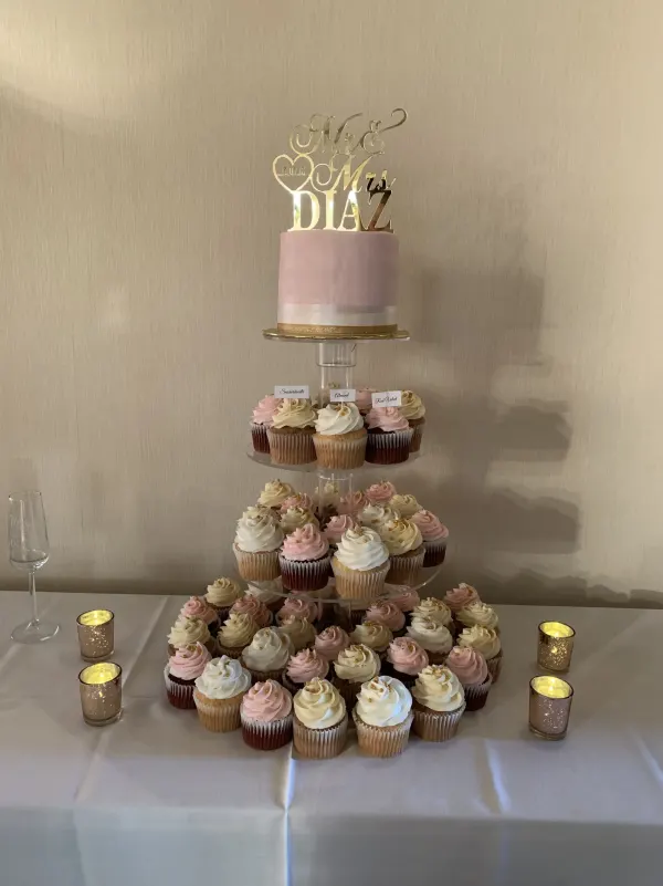 Pink fondant cake with a gold Mr and Mrs Diaz topper above tiers of pink and ivory cupcakes