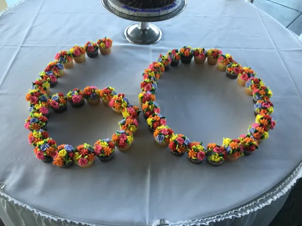 Cupcakes with multicolored buttercream flowers arranged as the number 60 on a white linen table
