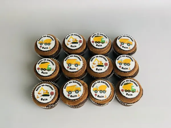 Chocolate frosted cupcakes topped with construction truck discs reading Happy 4th Birthday Quin