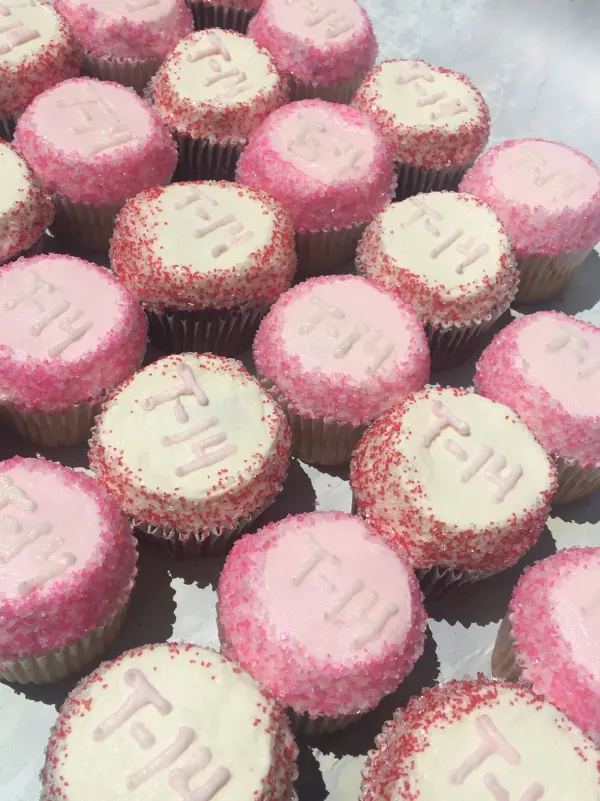 Pink and white buttercream cupcakes rimmed in sanding sugar and piped with the date 7-14