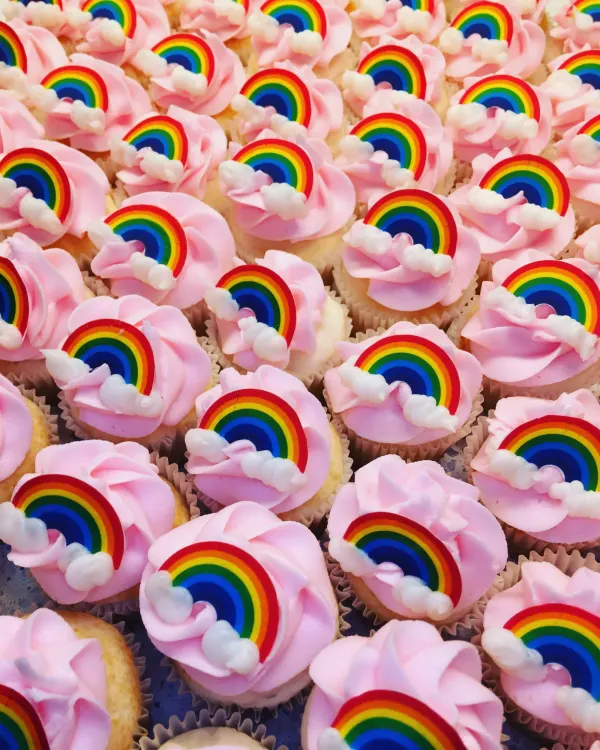 Tray of cupcakes with pink buttercream swirls and rainbow and cloud fondant toppers