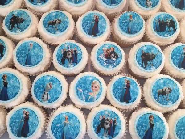 White cupcakes edged in sugar with Frozen image toppers of Elsa, Anna, Olaf and Sven