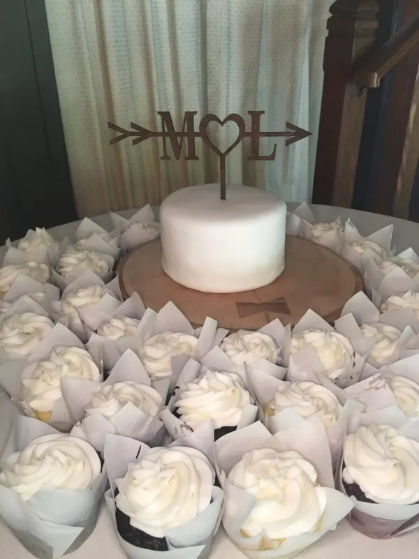 Small white fondant cake with a wooden M heart L topper ringed by white buttercream cupcakes