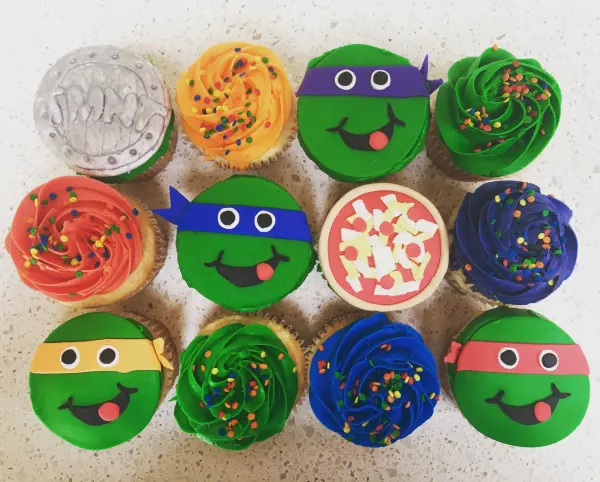 Dozen cupcakes with fondant ninja turtle faces in colored masks plus pizza and manhole designs