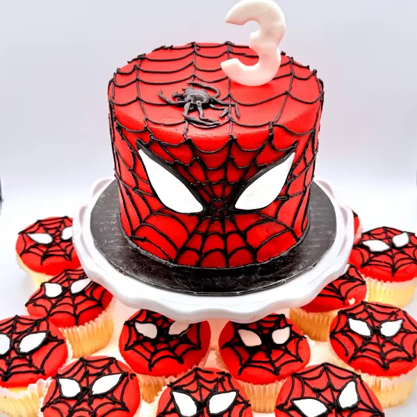 Spider-Man cake with a piped web, mask eyes and a number three, with matching web and mask cupcakes