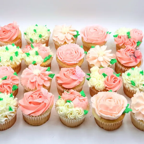 Floral cupcakes with piped roses, dahlias and hydrangeas in soft pink and cream with green leaves