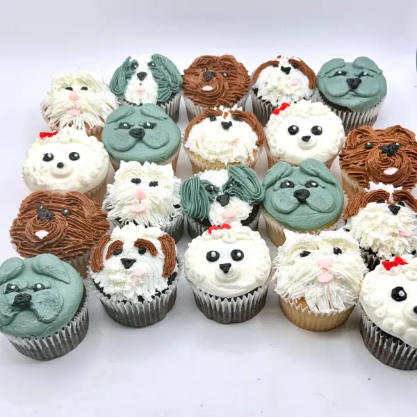 Puppy cupcakes piped as dogs in cream, grey and brown buttercream, each with its own face
