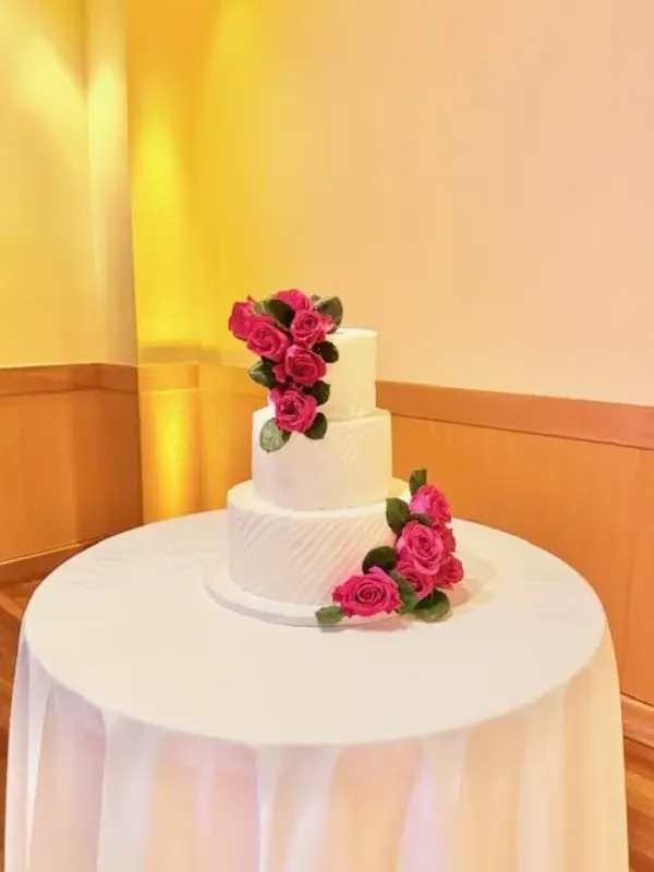 Elizabeth three-tier white wedding cake with hot pink roses cascading down two tiers and a combed texture on the base tier, 2026