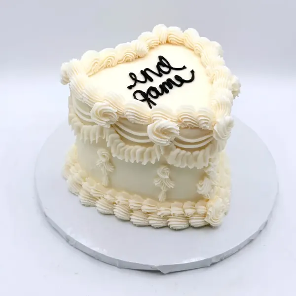 Cassandra heart-shaped ivory wedding cake in vintage lambeth piping with ruffles, shells and swags, finished with dark script lettering on top, 2025
