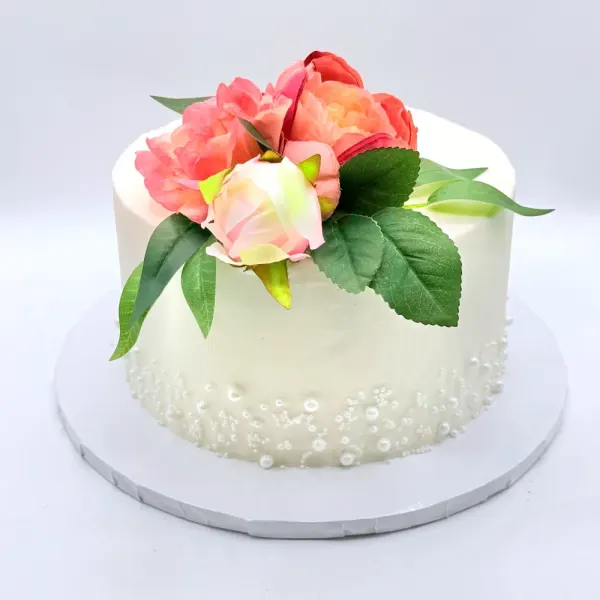 Ashley single-tier ivory wedding cake topped with coral and blush garden roses and green foliage, with piped pearls scattered around the base, 2025