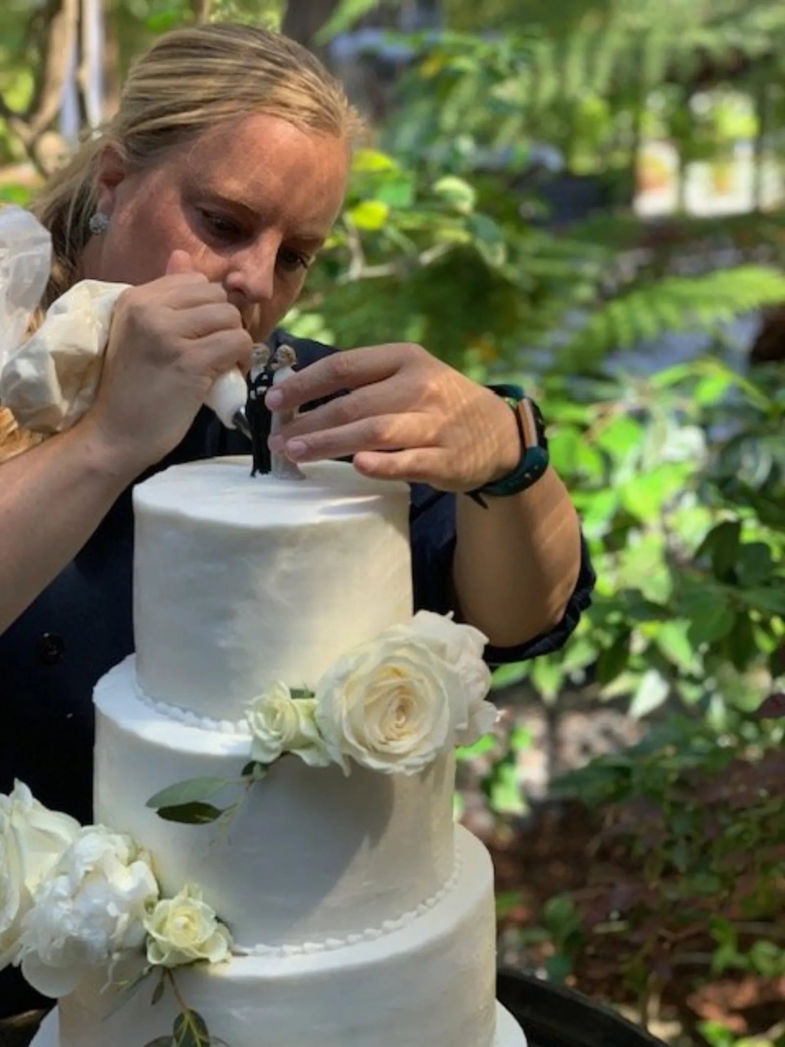 Lindsay Holdorf setting a bride-and-groom topper on a three-tier white wedding cake trimmed with garden roses